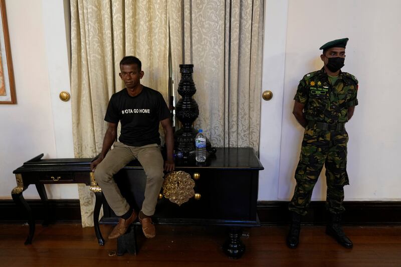 A Sri Lanka army officer stands guard as a protester sits on the table inside the official residence of President Gotabaya Rajapaksa. Photograph: Rafiq Maqbool/AP