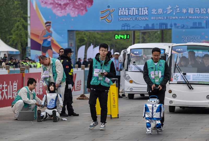 A humanoid robot is assisted by support technicians after collapsing while another runs by. Photograph: Kevin Frayer/Getty Images