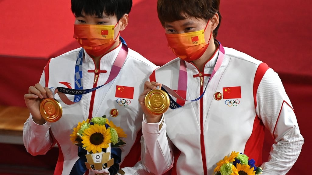 Gold medallists China’s Bao Shanju (L) and Zhong Tianshi pose with their medals on the podium with the badges on their tops. Photo: Greg Baker/AFP via Getty Images
