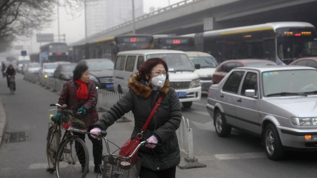 A woman (C) wearing a mask stands besides her bicycle as vehicles stop at a traffic junction on a busy street amid thick haze in Beijing: companies that specialise in making vehicle emissions cleaner are rushing to take advantage of Beijing’s war on pollution. Photograph: Barry Huang/Reuters