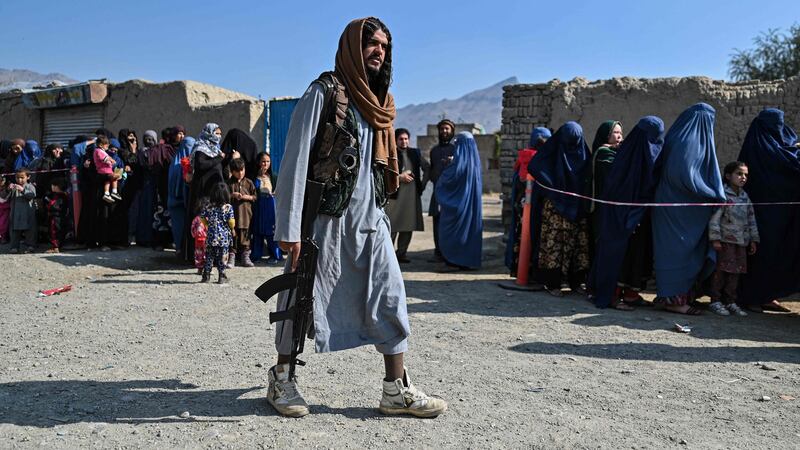 A Taliban fighter walks by women waiting in line for food on the outskirts of Kabul. Photograph: Hector Retamal/AFP