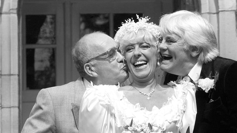 Coronation Street barmaid Bet Lynch (Julie Goodyear) getting a kiss from television groom Alec Gilroy (actor Roy Barraclough), and best man Charles Halliday (actor Tony Booth), after the TV wedding at the Holy Trinity Church in Bolton, Lancashire.  Photograph. PA Wire