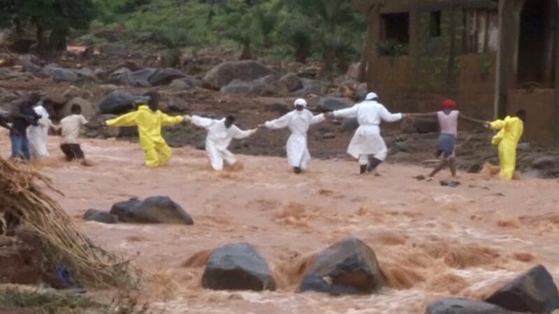 People wearing protective suits hold hands as they cross a river on Tuesday after a mudslide in the mountain town of Regent, Sierra Leone. Photograph: Reuters TV