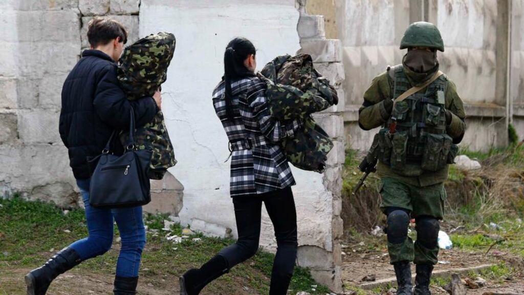 Two women, believed to be Ukrainian servicewomen, carry their uniforms as they walk past an armed man, believed to be a Russian serviceman, while leaving a military base in Perevalnoye, near the Crimean city of Simferopol, March 19, 2014. Ukraine’s National Security and Defence Council opened a session on Wednesday devoted to threats to national security following Russia’s moves to take control of the Crimea peninsula. REUTERS/Shamil Zhumatov