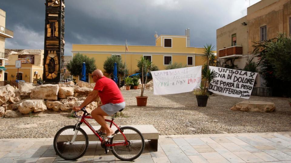 A man cycles past banners, which read: “An island full of pain that bears the indifference of the world” (right) and “Lampedusa wants to welcome immigrants alive, not dead”, in the centre of the southern Italian island of Lampedusa today. Photograph: Antonio Parrinello/Reuters