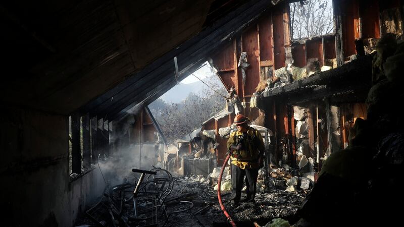 Captain Adrian Murrieta with the LAcounty fire department looks for hot spots on a wildfire-ravaged home. Photograph: Marcio Jose Sanchez/AP