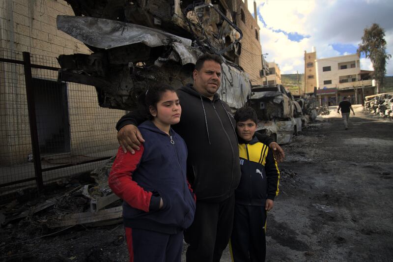 Sultan Abu Saries with his children Lamar (10) and Joud (eight) in front of cars burned during the attack on Huwara. Photograph: Hannah McCarthy