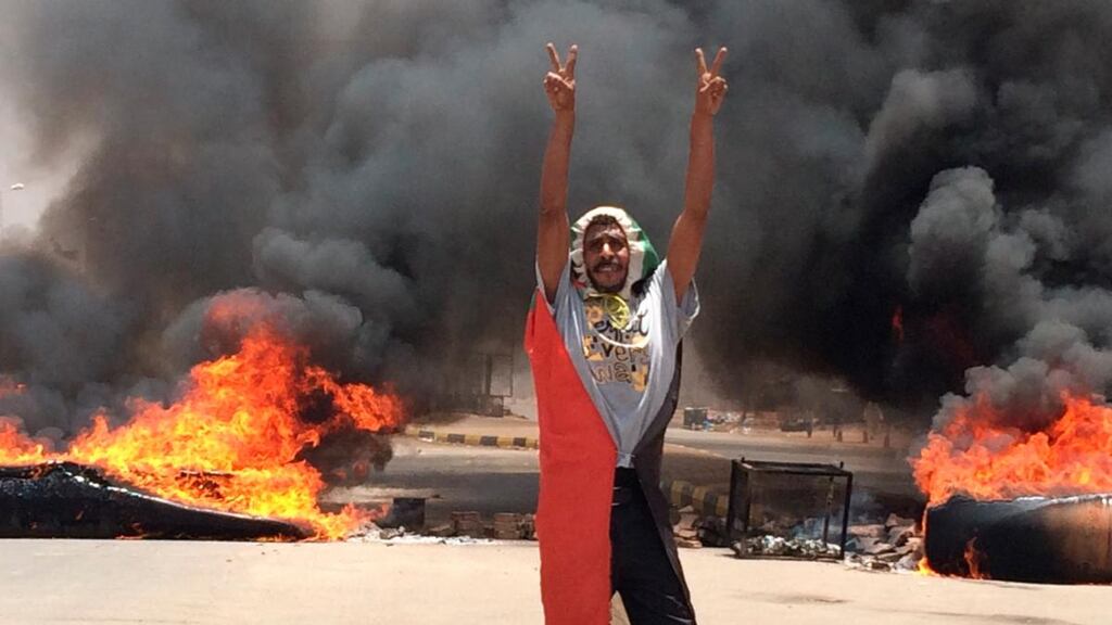A protester flashes the victory sign in front of burning tires and debris near the army headquarters in Khartoum, Sudan, on Monday. Photograph:  AP