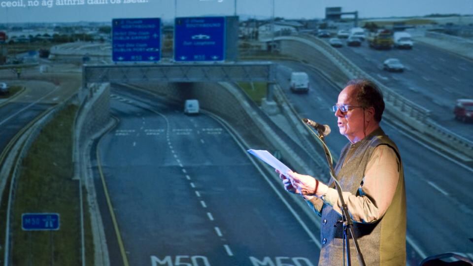 Paddy Bushe reads in front of a screen projection