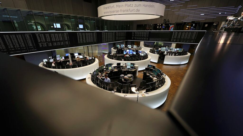 Traders work at their desks in front of the German share price index at the stock exchange in Frankfurt, German.