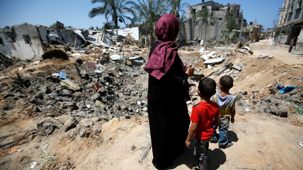 A Palestinian mother and her sons survey the rubble of a destroyed home in Deir Al-Balah, in the central Gaza Strip. The funeral for seven members of the family whose house was attacked in an Israeli airstrike was held yesterday. Photograph: Mohammed Saber/EPA