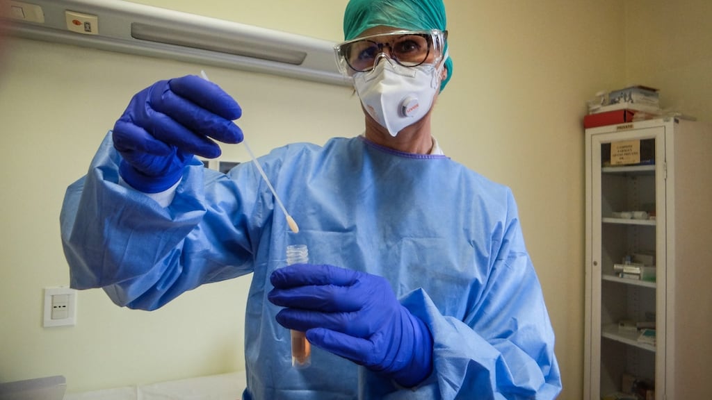A healthcare professional wears a protective suit and a face mask while inspecting a vial containing a swab sample for the novel coronavirus. Photograph: Matteo Corner/EPA
