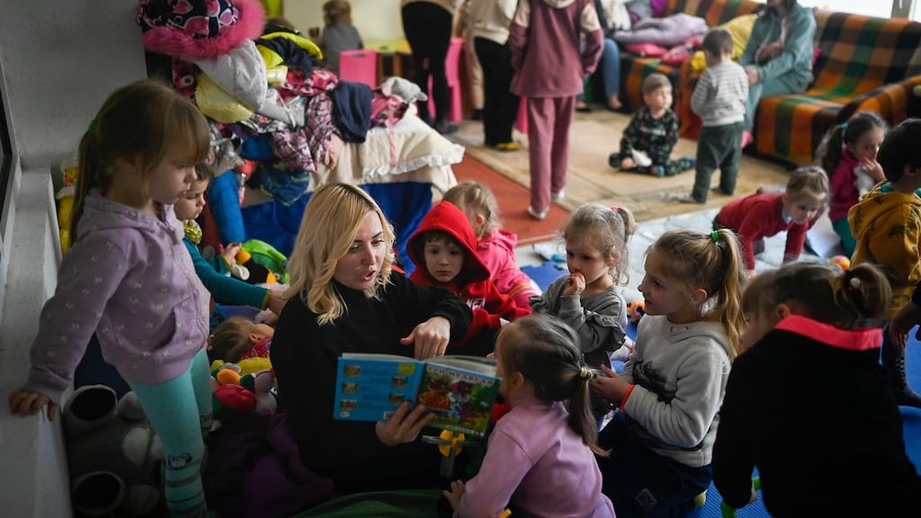 A woman reads a book to Ukrainian children in a playground at a summer camp, turned into a refugee center in the tiny resort town of Kiten, on Bulgaria’s Black Sea coast. Photograph: Nikolay Doychinov/AFP via Getty Images