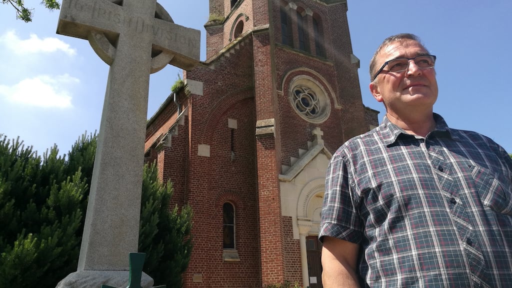 Mayor of Guillemont Didier Samain in front of the granite cross memorial to the 16th (Irish) Division in the village.