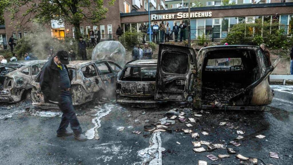 A bystander checks the debris around a row of burnt cars in the Stockholm suburb of Rinkeby. Photograph: Fredrik Sandberg/Scanpix/Reuters