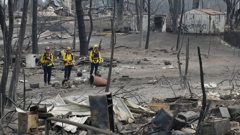 San Bernardino County Fire department firefighters assess the damage to a neighbourhood in the aftermath of a wildfire on Sunday. Photograph: Marcio Jose Sanchez/AP