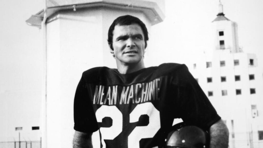 American actor Burt Reynolds holds a helmet while standing in a ‘Mean Machine’ football jersey in a still from the film, The Longest Yard, directed by Robert Aldrich, 1974. Photo: Paramount Pictures/Courtesy of Getty Images