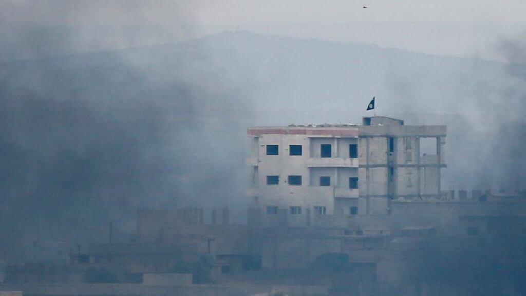 A black flag belonging to the Islamic State is seen through smoke on top of a house in the Syrian town of Kobani yesterday. Photograph: Kai Pfaffenbach/Reuters