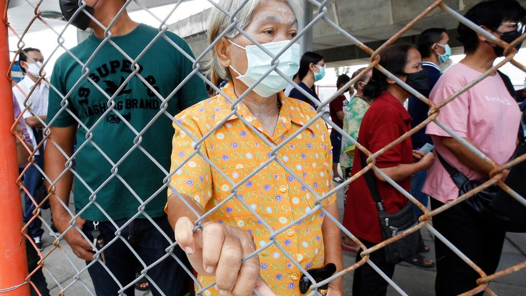 A woman clings a fence for support in crowds waiting to be vaccinated against Covid-19 in Bangkok. Photograph: Narong Sangnak