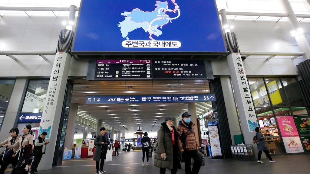 Passengers walk under a monitor displaying information on the coronavirus, at Suseo Station in Seoul, South Korea.