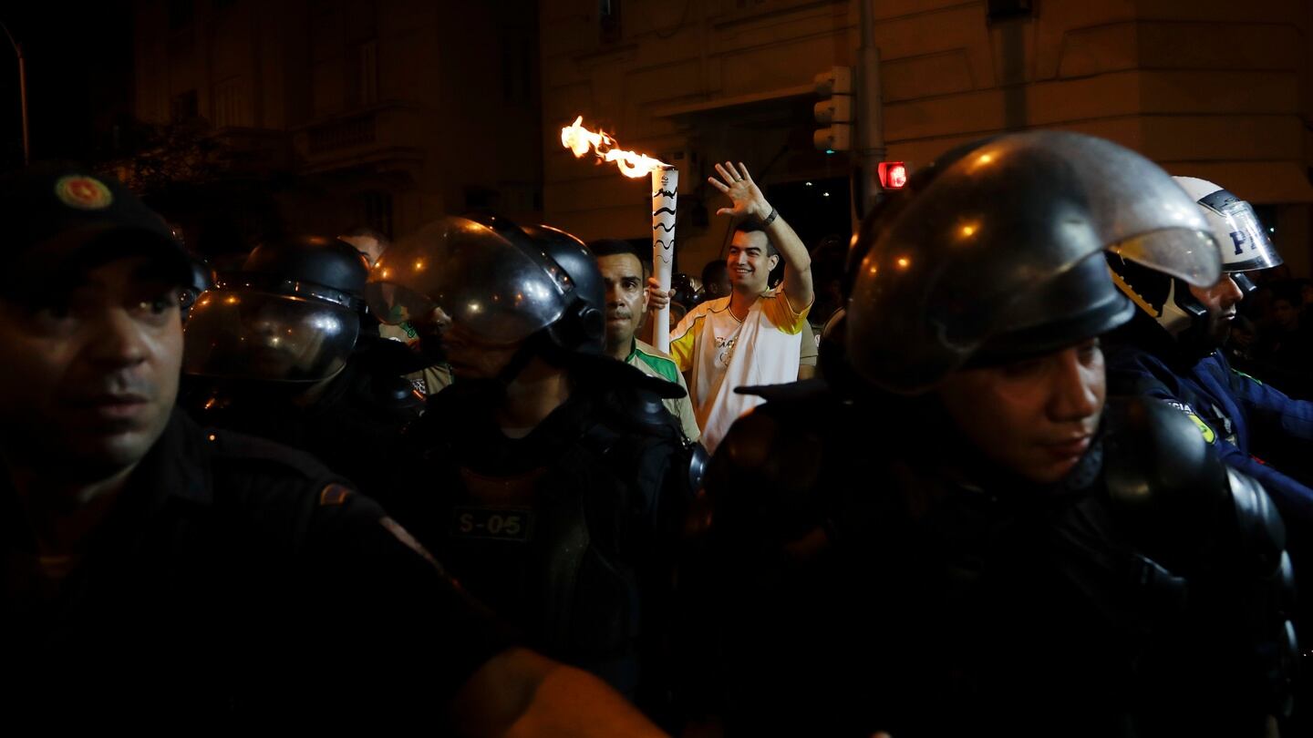A man carries the Olympic torch surrounded by police along the streets of Copacabana. Photograph: AP / Gregory Bull