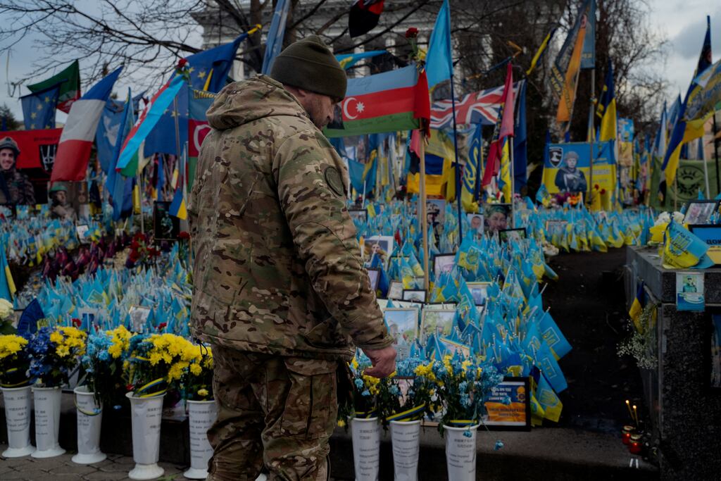 A soldier at the makeshift memorial to Ukrainian and foreign fighters leaves cigarettes next to a photo of his comrade on Independence Square in Kyiv. Photograph: Tetiana Dzhafarova/AFP
