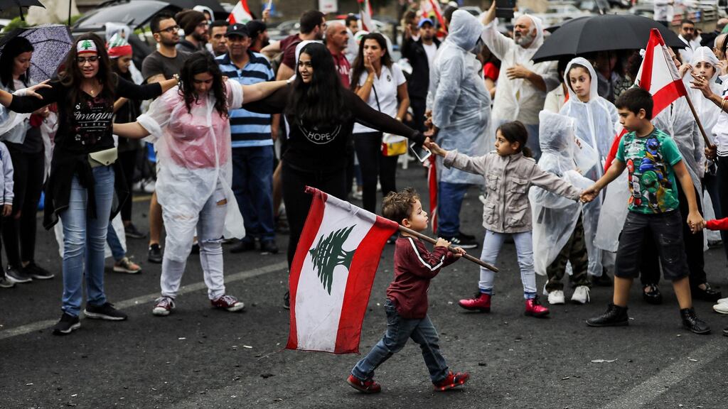A boy walks with a Lebanese flag past protesters in Zouk Mosbeh, north of Beirut, on Thursday. Photograph: Joseph Eid/AFP via Getty Images