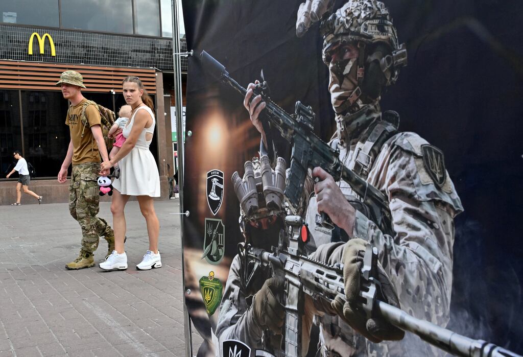 A Ukrainian serviceman and his partner carrying a baby walk past a recruiting point of the 4th Brigade of the Operational Assignment 'Rubizh' in Kyiv on July 4th, 2024, as the Russian war on Ukraine continues. Photograph: Sergei Supinsky/AFP/Getty