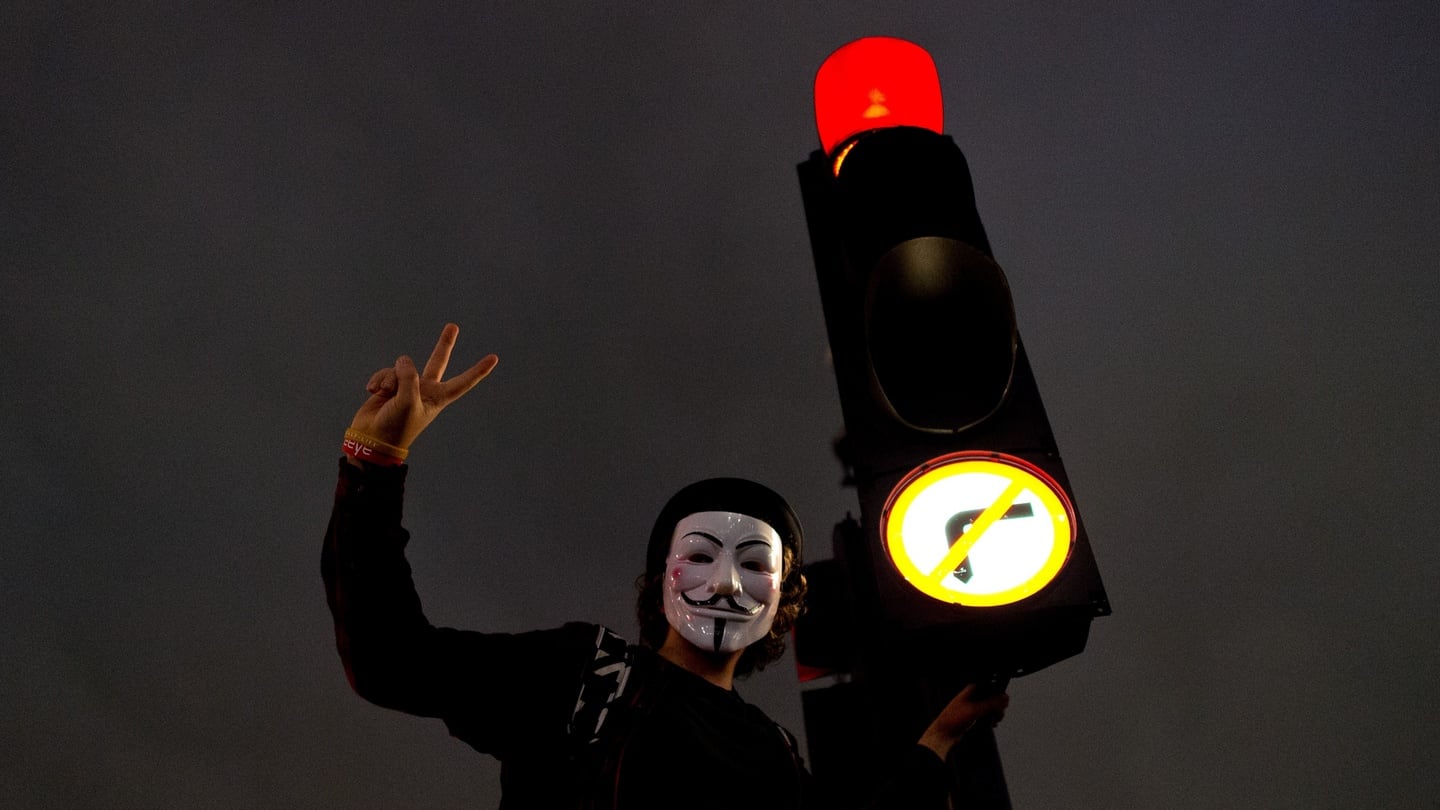 A masked protester climbs a traffic light in Parliament Square during the Million Mask March in London. Photograph: Getty