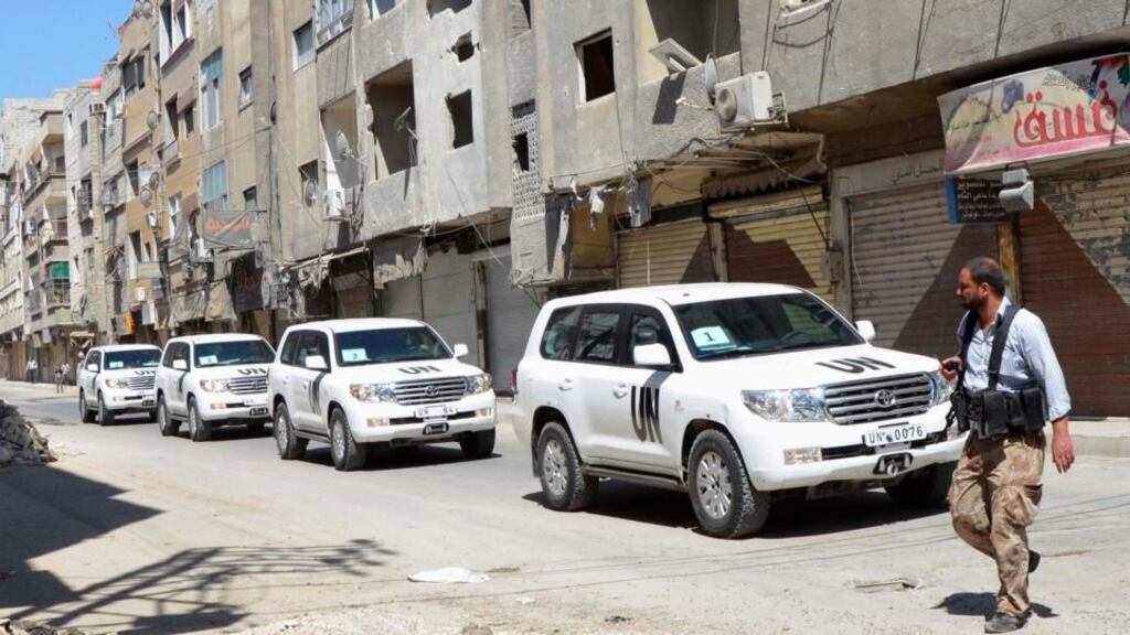 A Free Syrian Army fighter passes by the convoy of U.N. vehicles carrying a team of United Nations chemical weapons experts