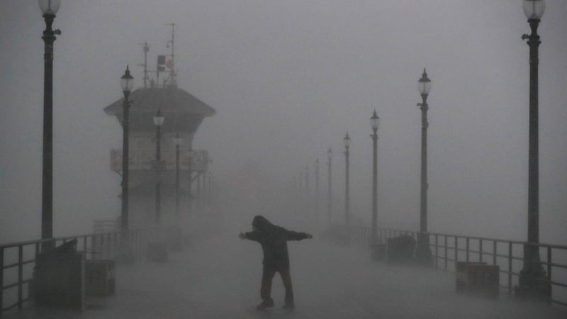 A man struggles against gusty wind and heavy rain as he walks along a pier in Huntington Beach, California on Friday. Photograph: AP