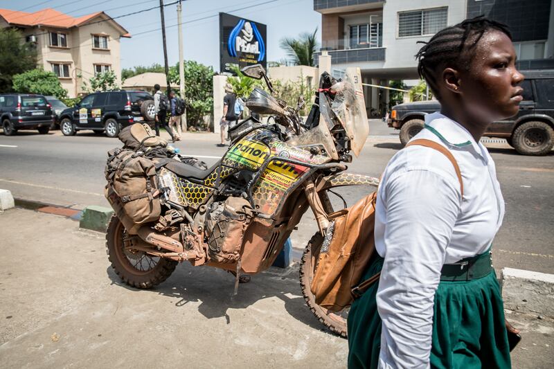 A Sierra Leonean schoolgirl walks past a motorbike that was driven as part of the Budapest to Bamako rally. Photograph: Sally Hayden