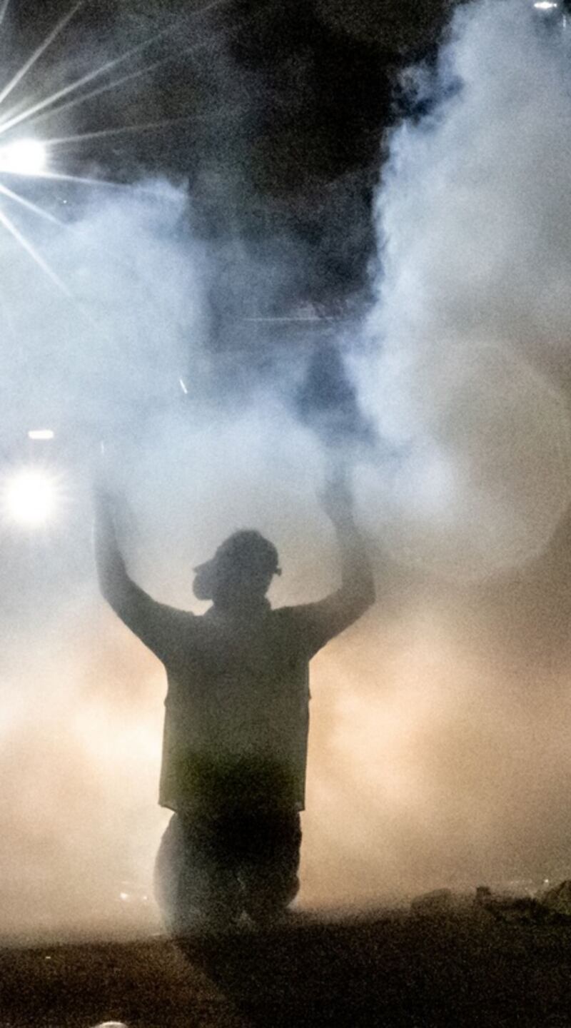 A demonstrator kneels and holds up his arms as police fires tear gas in front of the Brooklyn Center Police Station. Photograph: Kerem Yucel/AFP