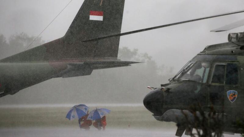 Indonesian Air Force crew members taking part in the search for AirAsia QZ8501 wait out a rain storm under the tail of a cargo plane at the airbase in Pangkalan Bun, Central Kalimantan on Sunday. Photograph: Darren Whiteside/Reuters
