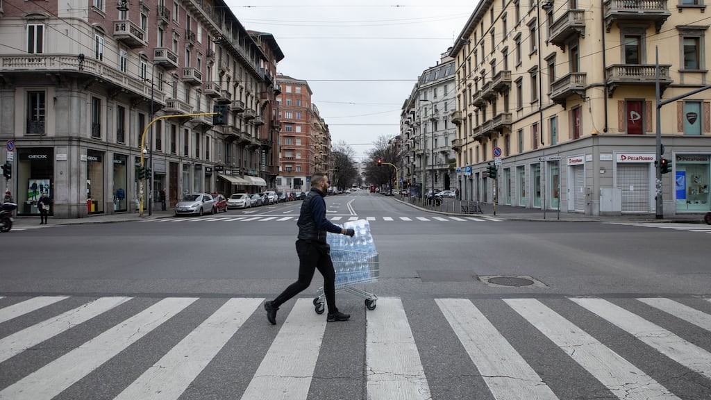 A man, pulling a trolley filled with bottles of water, crosses a deserted street on in Milan, Italy on Thursday. Photograph: Emanuele Cremaschi/Getty Images)