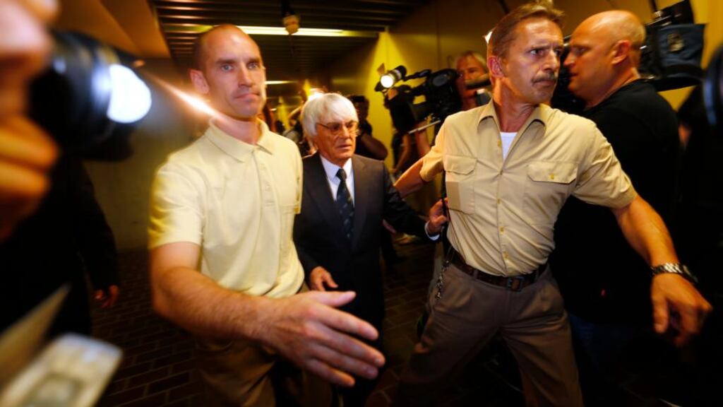 Formula One chief executive Bernie Ecclestone is escorted past the waiting media as he leaves after his trial at the regional court in Munich today. A German judge said he would discontinue for now a bribery trial against Mr Ecclestone. Photograph: Reuters