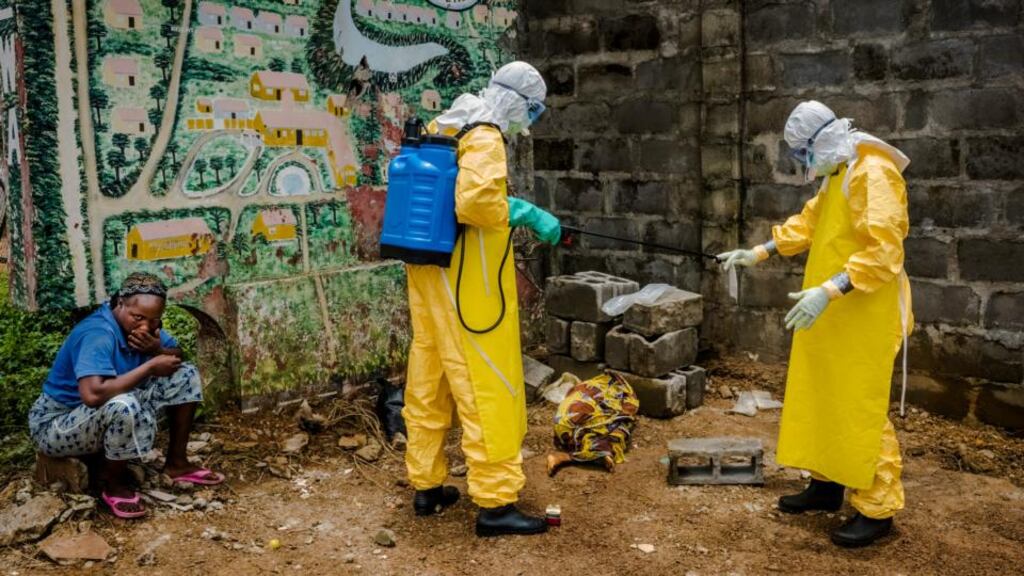 Doctors Without Borders workers disinfect a  plastic bag containing a blood sample from Hawa Konneh (9)  as she lies wrapped in a shawl in the Liberian capital Monrovia, as her mother, Masogbe, looks on. Photograph: Daniel Berehulak/New York Times