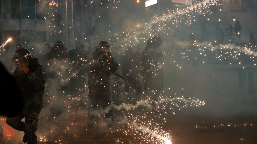 Lebanese riot policemen react to firecrackers fired by the supporters of the Shiite Hezbollah and Amal Movement groups, as they try to attack the anti-government protesters squares, in downtown Beirut, Lebanon, Saturday, Dec. 14, 2019. (AP Photo/Hussein Malla)
