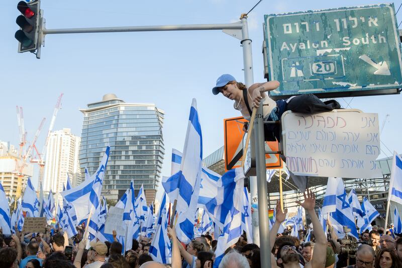 An anti-government protester climbing a streetlight  in Tel Aviv. Photograph: Amit Elkayam/The New York Times