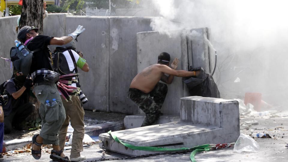 Thai anti-government protesters and tear gas as they throw stones and drag back the concrete barricades around Government House. Photograph: Rungroj Yongrit/EPA