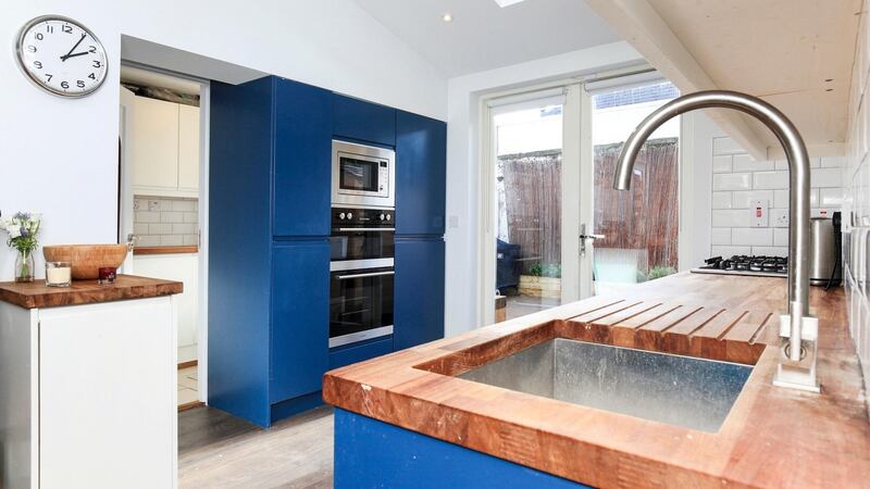 The kitchen has Prussian blue units and timber countertops with double doors opening out to a decked yard to the rear