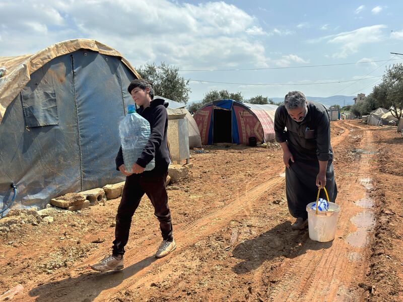 Hussein and his 12 year old son Mudar carry water to their family tent across muddy roads