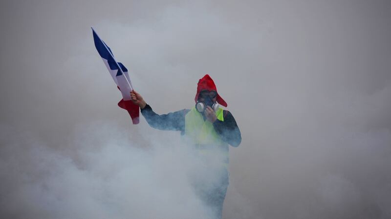 A demonstrator holds up a furled French flag amid billowing tear gas during a “gilets jaunes” (yellow vests) protest against rising oil prices and living costs in Paris. Photograph: AFP/Getty Images