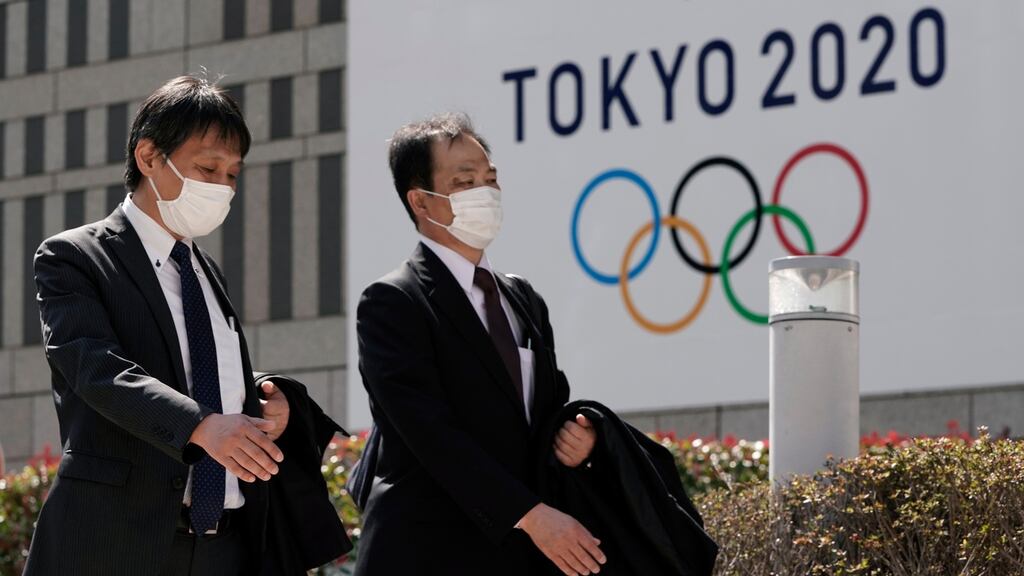 Office workers wearing masks walk past the emblem of Tokyo 2020 Olympics. Photo: Kimimasa Mayama/EPA