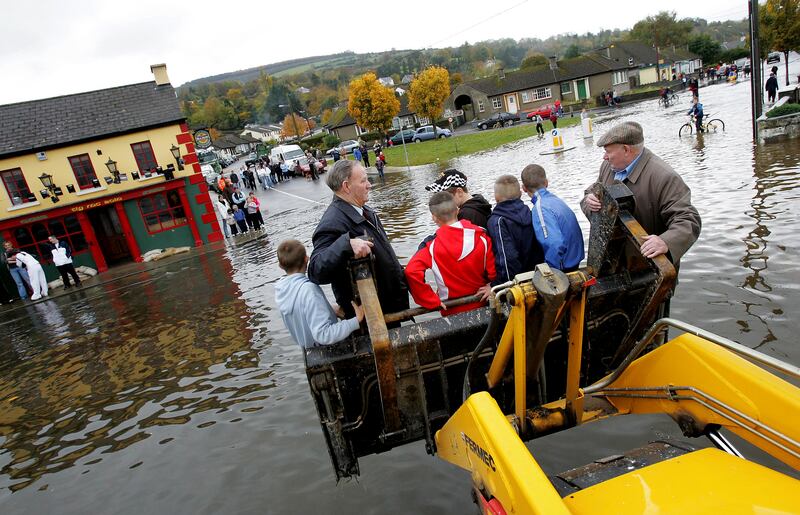 Passengers in the bucket of a digger hitch a ride across the Old Bridge where the banks of the Suir burst in Clonmel. Photograph: Brenda Fitzsimons