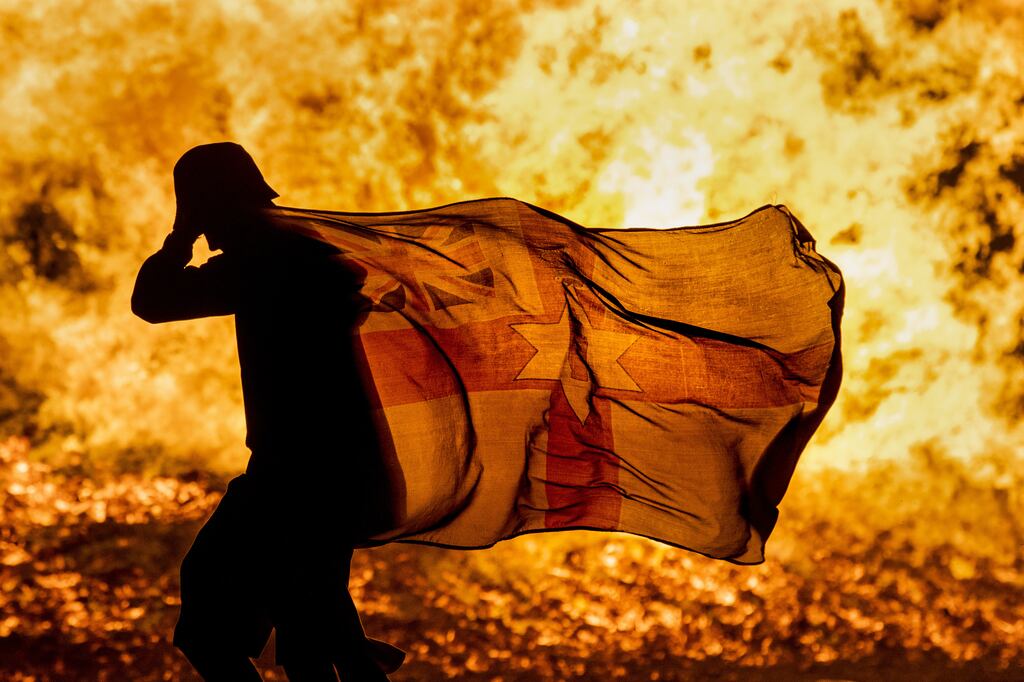 A man carries a Northern Ireland flag past the burning Craigyhill loyalist bonfire in Larne, Co Antrim on Monday night.