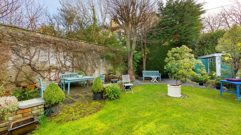 The wide rear garden is sheltered by a high wall and is prettily laid out in lawn, with mature trees and bushes and a patio by the back wall