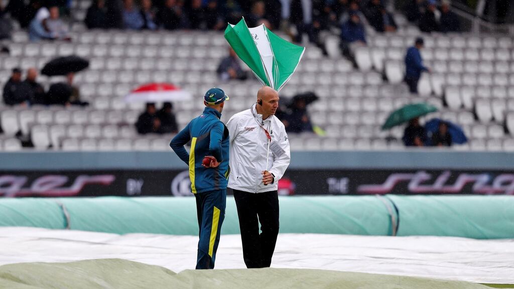 The umbrella of umpire Alex Wharf is blown inside out as he stands in the rain with Australia’s Nathan Lyon whilst covers protect the pitch at Lord’s. Photo: Adrian Dennis/Getty Images