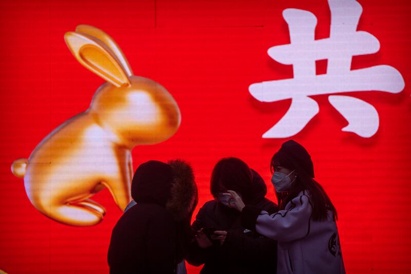 People wearing masks stand in front of a large screen displaying a graphic decoration for the upcoming Lunar New Year in Beijing. Photograph: Mark Schiefelbein/AP