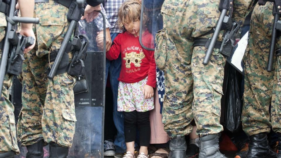A young girl peeks out between the lines of Macedonian police forces, while waiting to board a bus after crossing the Macedonian-Greek border near Gevgelija. More than 10 thousands refugees and migrants arrived in Piraeus from the overcrowded Greek islands in the last 24 hours. Photograph: Robert Atanasavoski/AFP/Getty Images